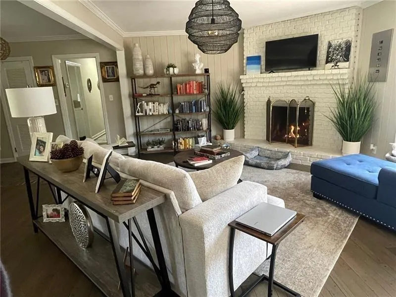 Living room with ornamental molding, a brick fireplace, wood walls, a chandelier, and wood finished floors