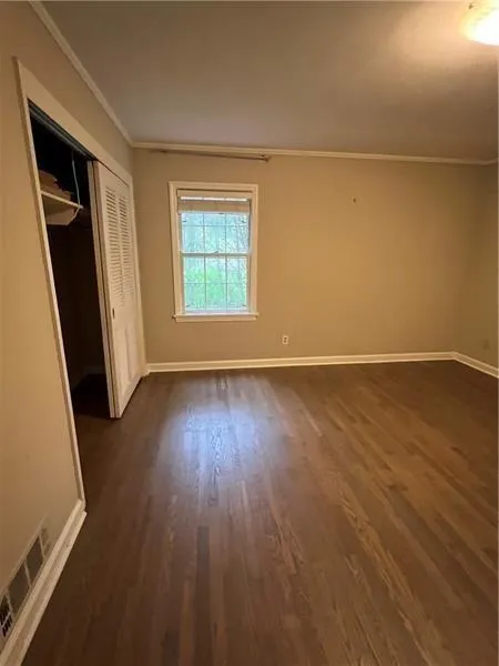 Unfurnished bedroom featuring crown molding, a closet, and dark wood-style floors