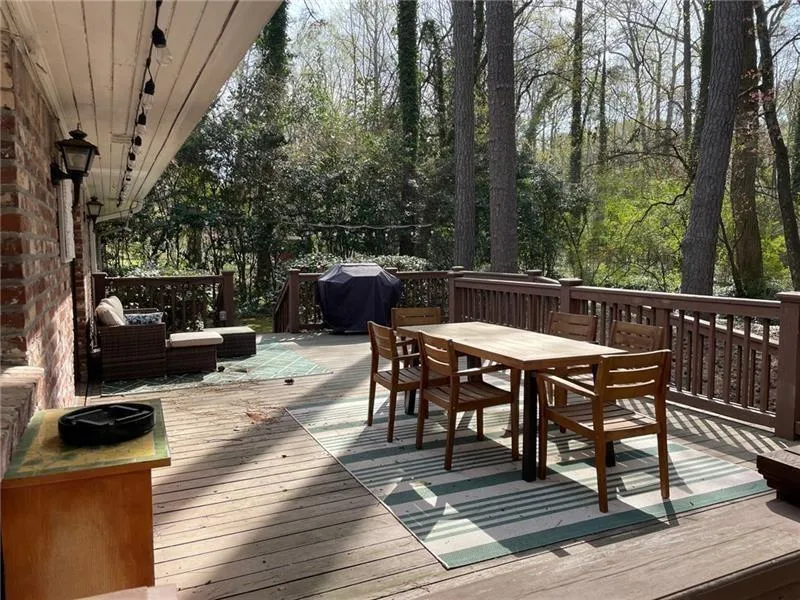 Wooden terrace featuring outdoor dining space, grilling area, and view of scattered trees