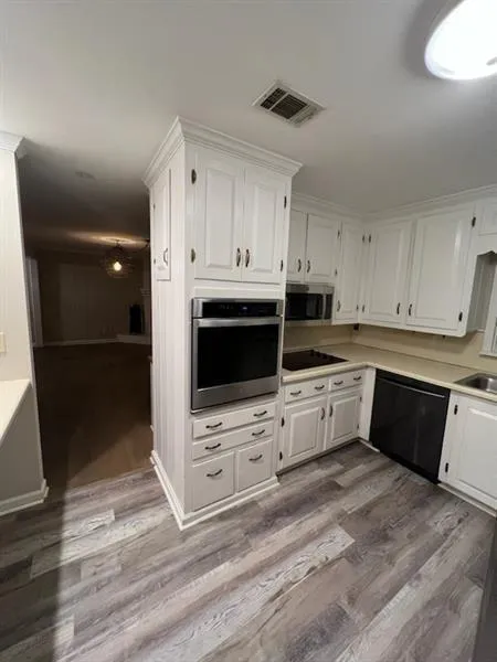 Kitchen featuring white cabinetry, black appliances, light countertops, and light wood finished floors