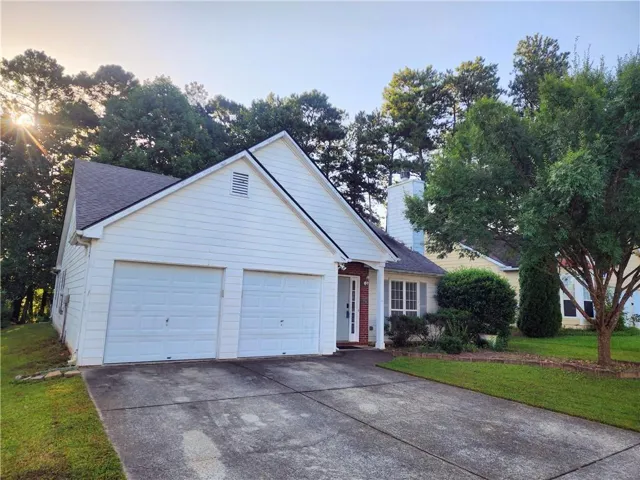 White siding exterior with a two-car garage, concrete driveway, and mature landscaping