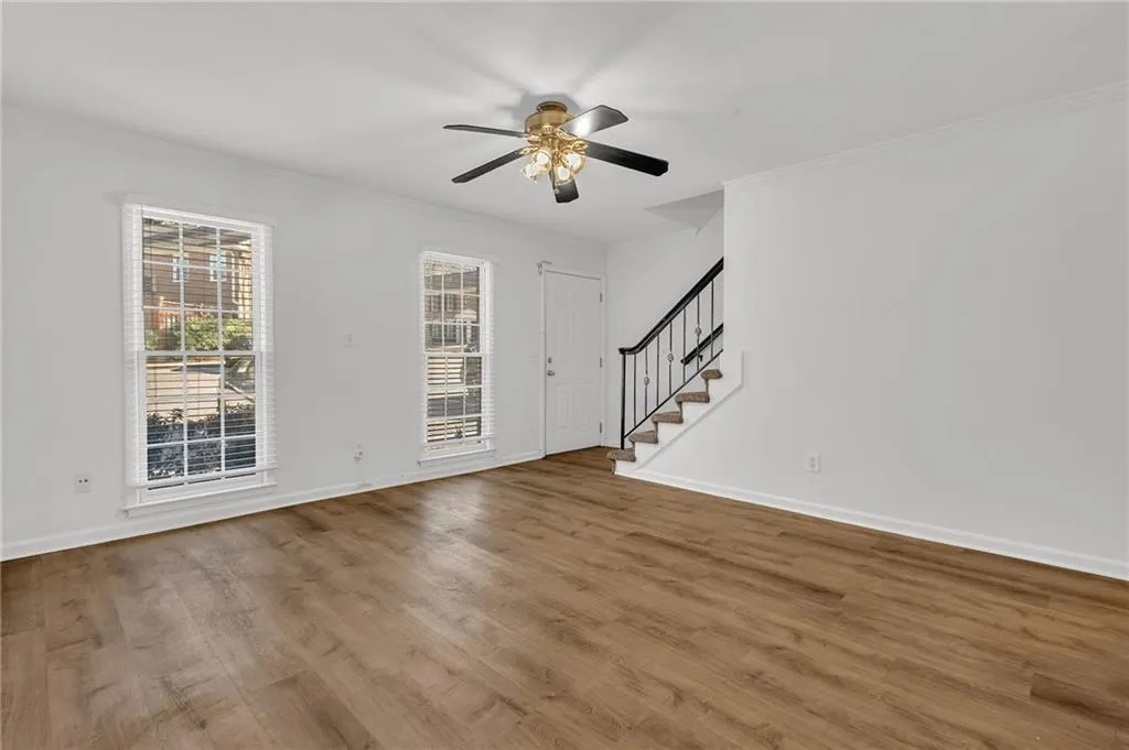Unfurnished living room with stairs, crown molding, wood finished floors, and a ceiling fan