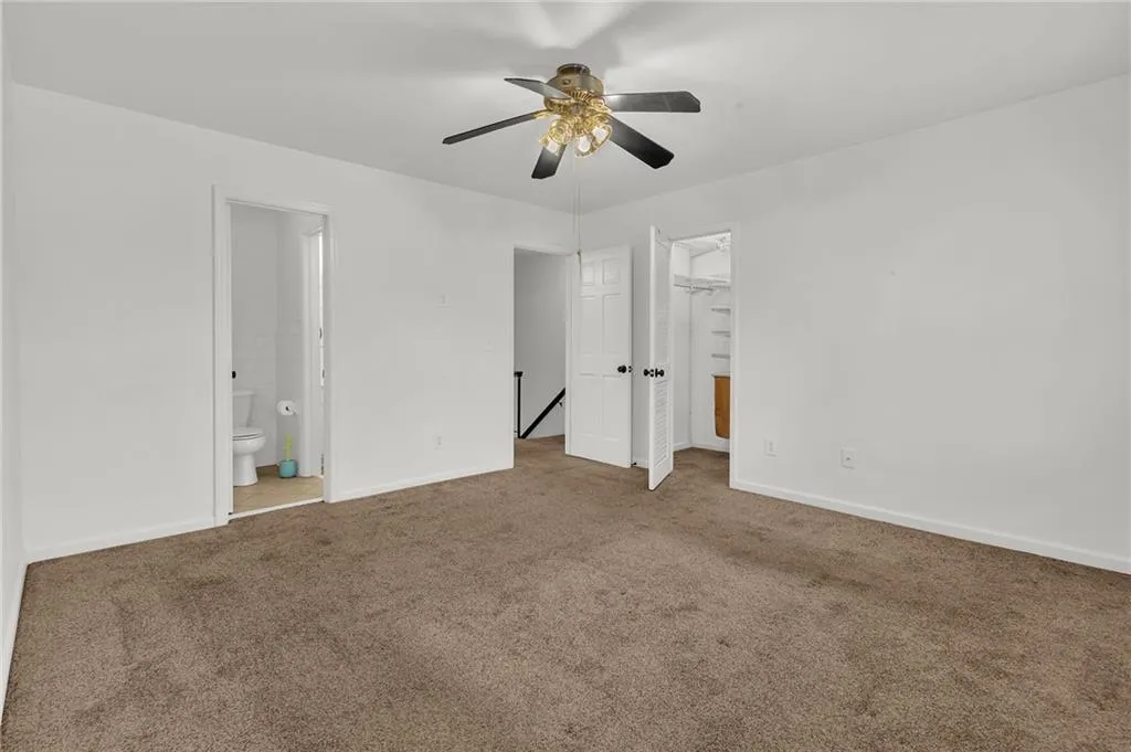 Unfurnished bedroom with carpet floors, a spacious closet, a ceiling fan, and ensuite bathroom