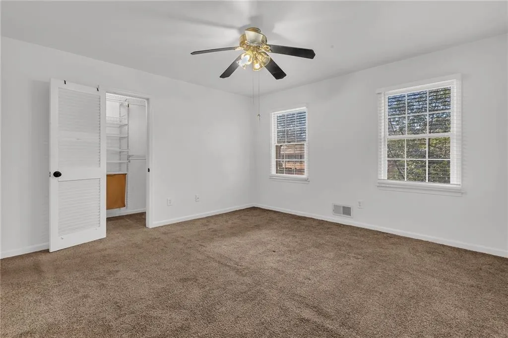 Unfurnished bedroom with a walk in closet, carpet flooring, and a ceiling fan