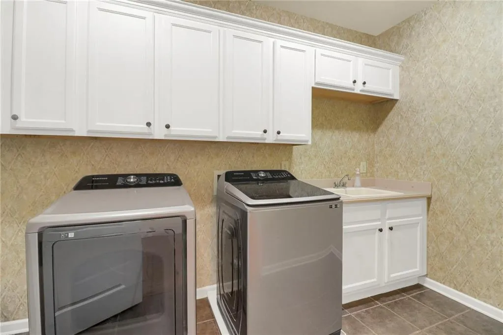 Washroom featuring wallpapered walls, washing machine and clothes dryer, cabinet space, and dark tile patterned flooring