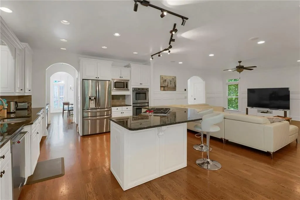 Kitchen with arched walkways, stainless steel appliances, recessed lighting, white cabinets, and a center island