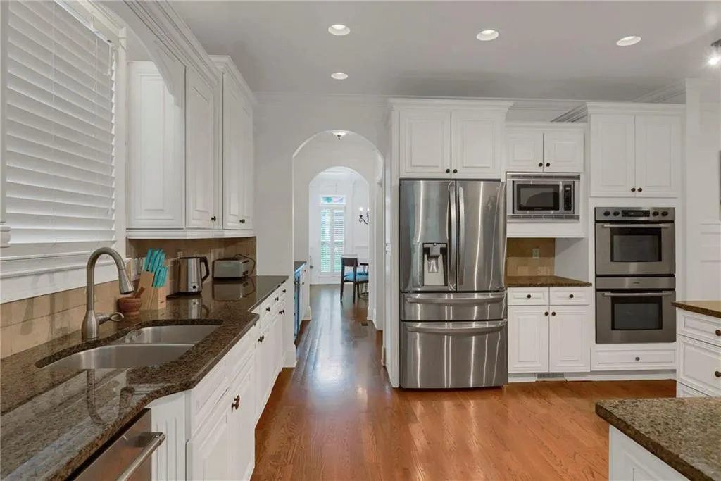 Kitchen featuring arched walkways, tasteful backsplash, appliances with stainless steel finishes, crown molding, and wood finished floors