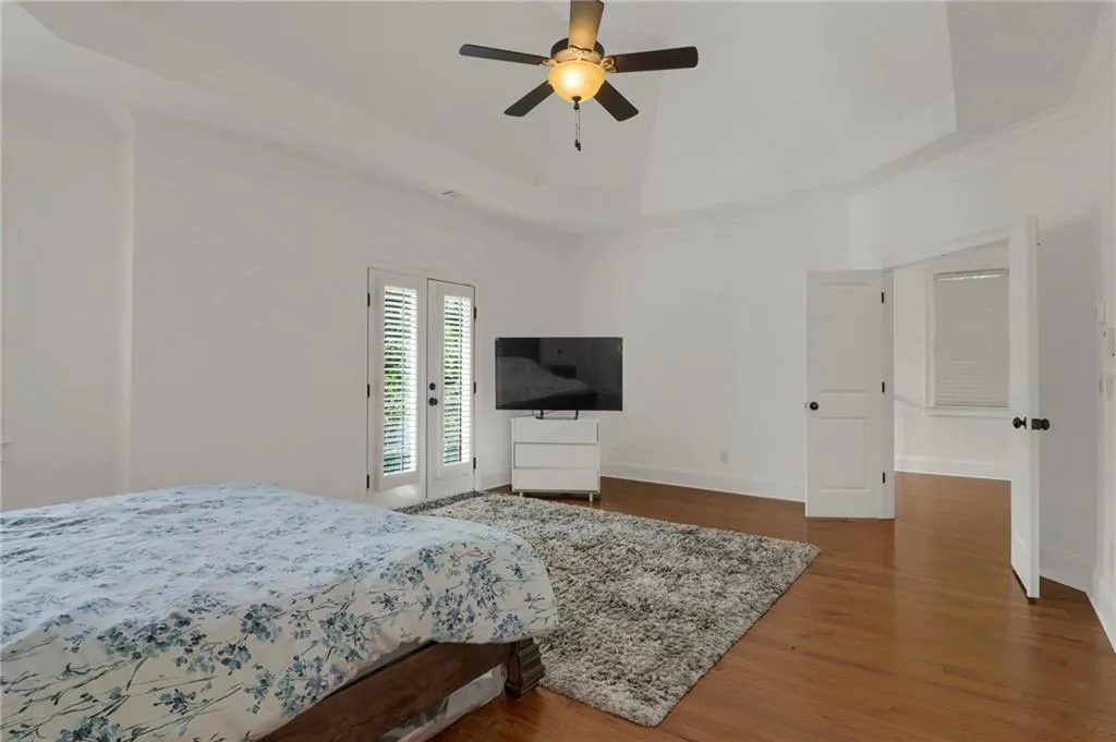 Bedroom with a tray ceiling, wood finished floors, access to outside, ceiling fan, and ornamental molding