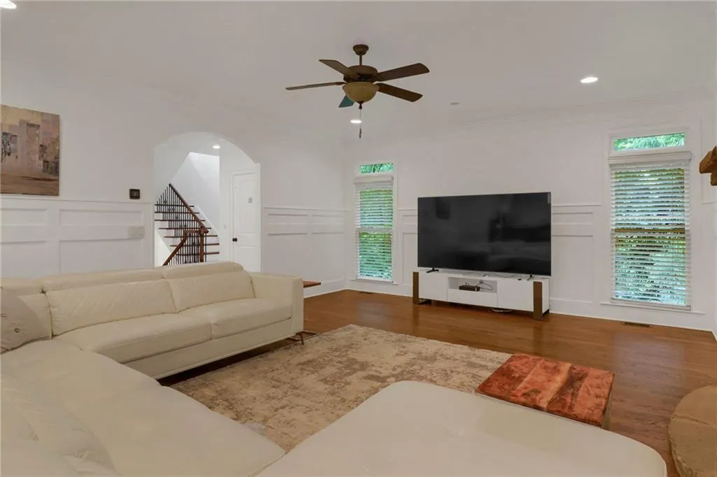 Living room with a decorative wall, wood finished floors, recessed lighting, ceiling fan, and stairs