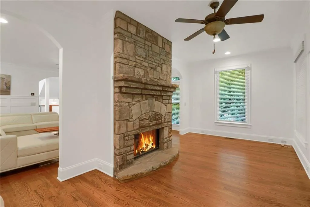Unfurnished living room featuring arched walkways, wood finished floors, ornamental molding, a stone fireplace, and recessed lighting