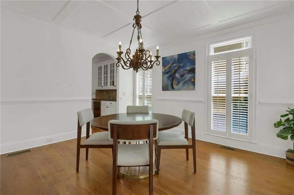Dining area with wood finished floors, a chandelier, coffered ceiling, arched walkways, and crown molding