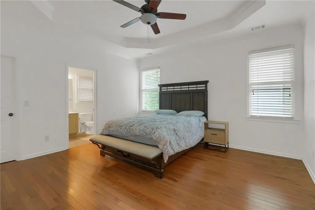 Bedroom featuring light wood-type flooring, a tray ceiling, ensuite bathroom, a ceiling fan, and ornamental molding