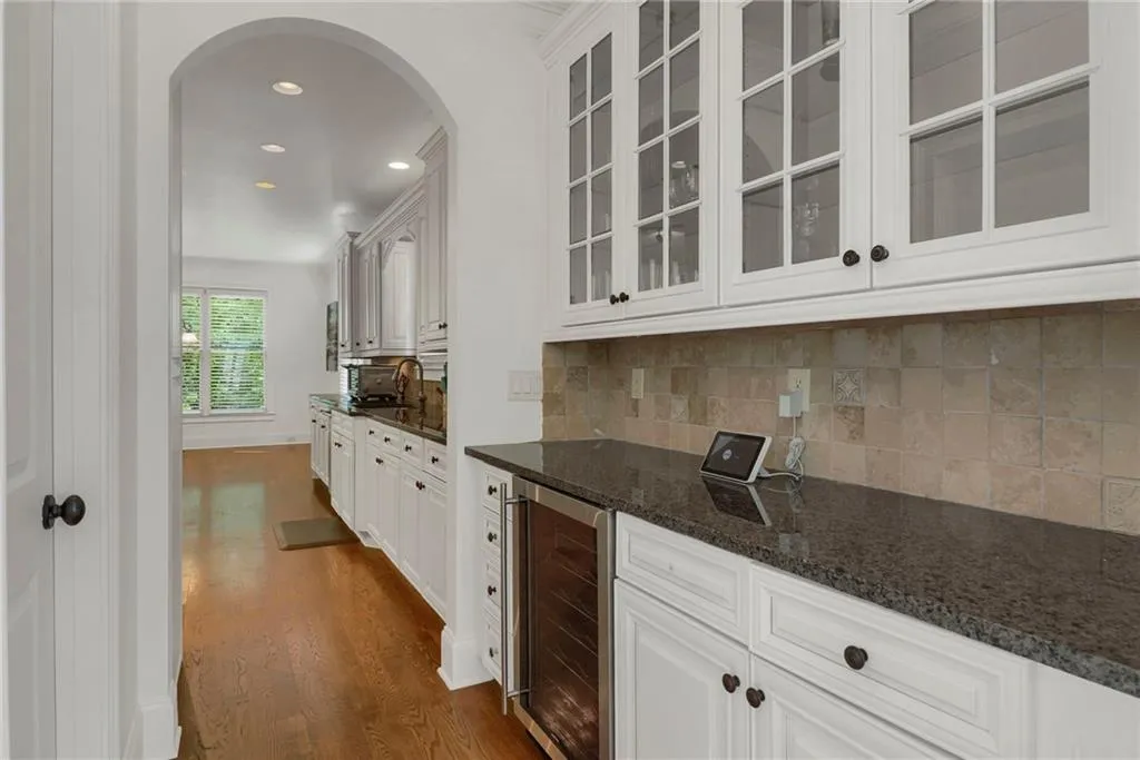 Bar area with arched walkways, beverage cooler, recessed lighting, dark wood-style floors, and decorative backsplash