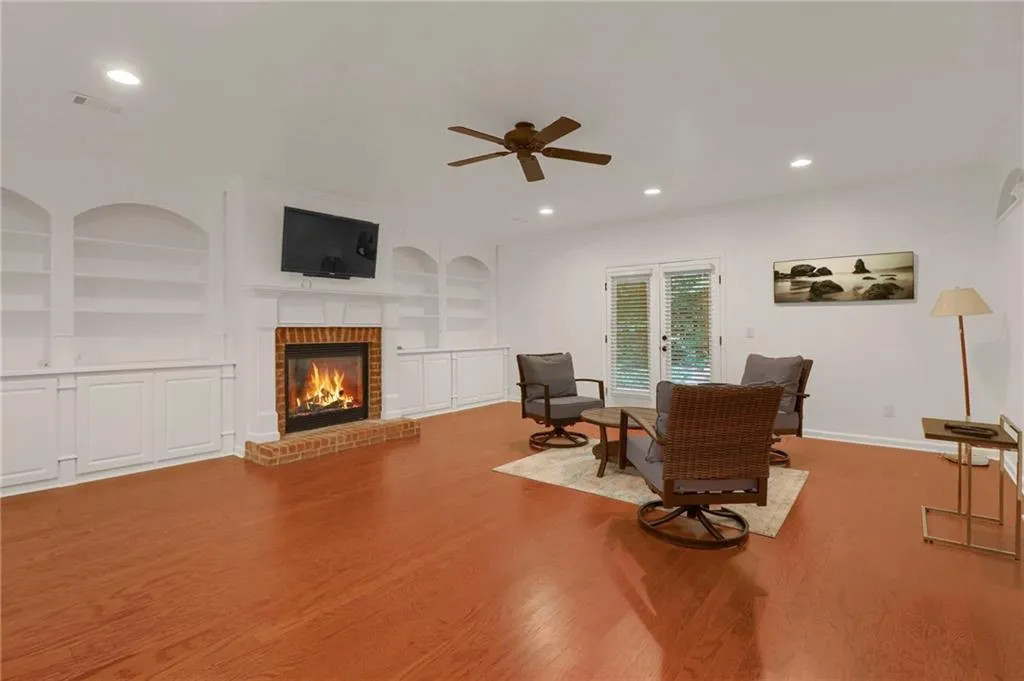 Living area with built in features, recessed lighting, wood finished floors, a brick fireplace, and ceiling fan