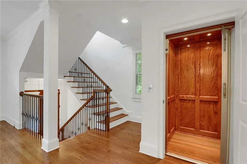 Staircase with wood finished floors, ornamental molding, and elevator