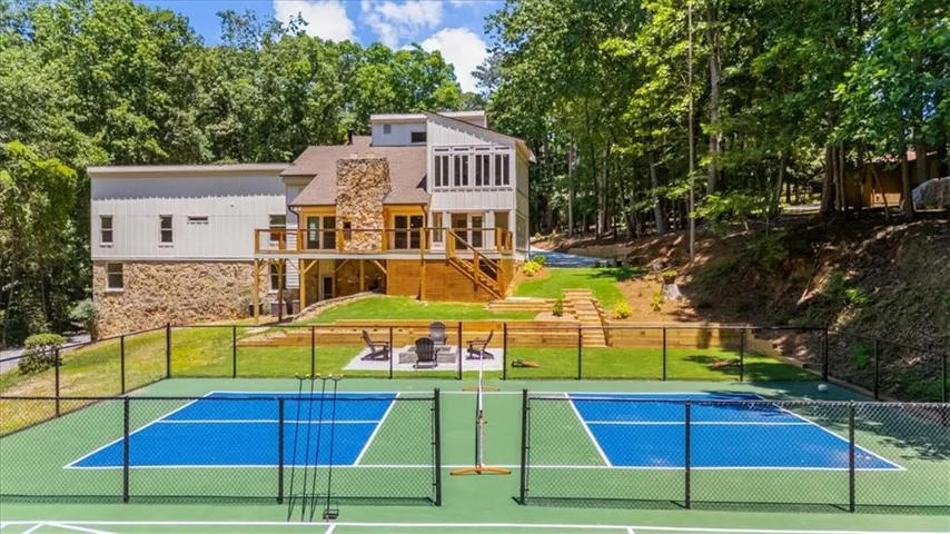 Expansive outdoor amenities featuring two fenced pickleball courts, a dedicated fire pit area with seating, a multi-level terraced lawn, and a stone and siding exterior with multiple exterior decks