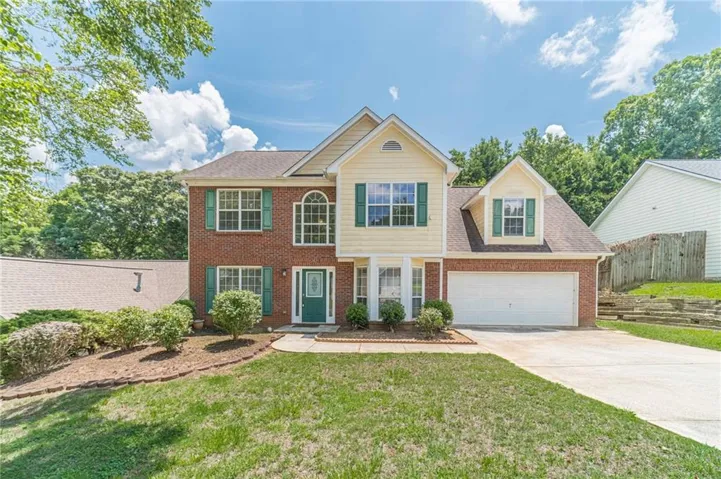 Two-story brick and siding home featuring a two-car garage, green front door, and mature landscaping