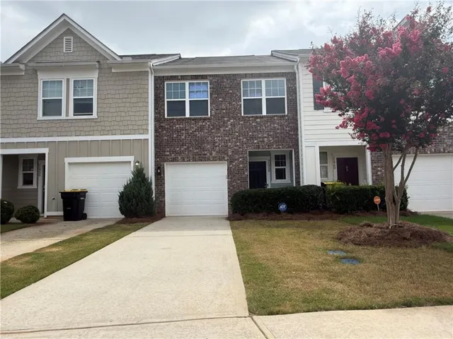 Brick and siding townhouse exterior featuring a concrete driveway, attached garage, and mature landscaping