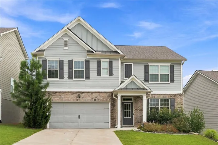 Two-story residence featuring light gray siding, brick accents, dark gray shutters, a two-car garage, and a covered entry