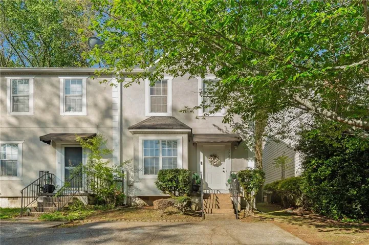 Stucco exterior with multiple windows, front entry with awning, bay window, and established trees