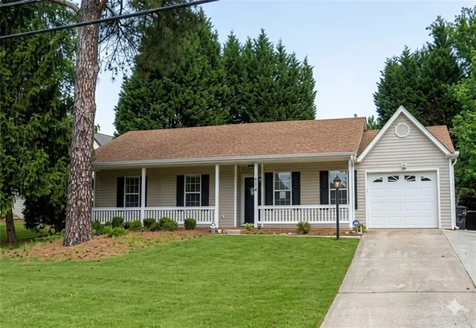 Front exterior featuring a covered porch with white railing, light-colored siding, an attached garage, a paved driveway, and mature landscaping