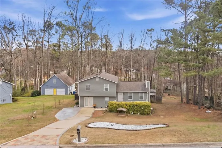 Split level home featuring driveway, a front lawn, a chimney, and view of wooded area