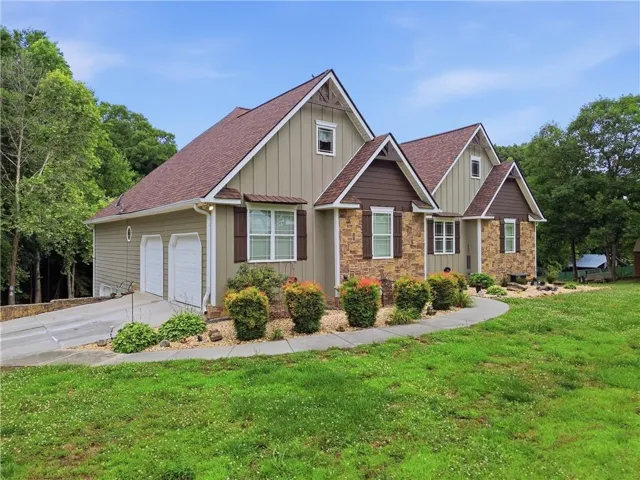 Craftsman-style exterior with stone and vertical siding accents, a two-car garage, multiple gables, and a curved walkway