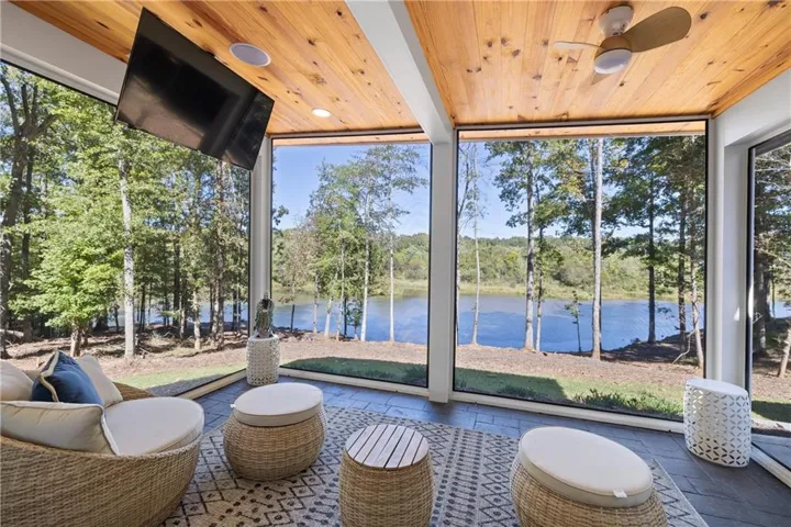 Screened porch featuring a natural wood plank ceiling, an integrated ceiling fan, and large windows overlooking a body of water
