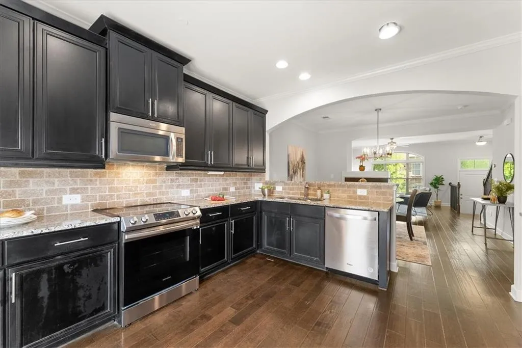 Kitchen featuring hanging light fixtures, backsplash, kitchen peninsula, dark hardwood / wood-style flooring, and stainless steel appliances