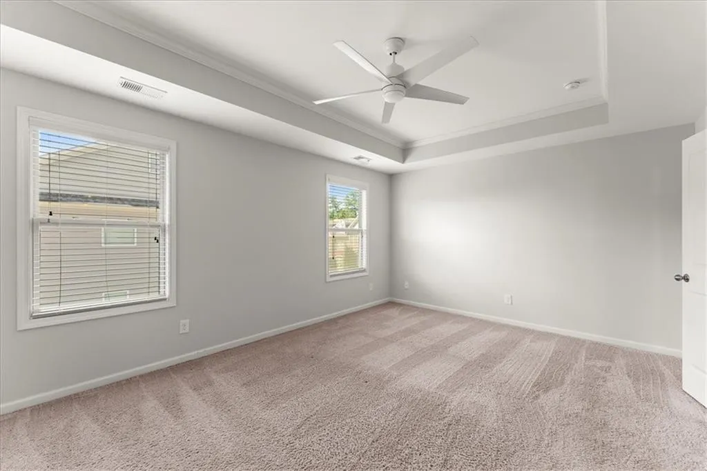 Carpeted primary bed room with ceiling fan, a tray ceiling, and crown molding