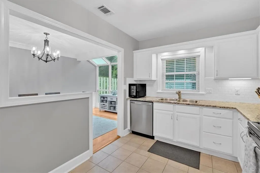 Kitchen with stainless steel dishwasher, a sink, white cabinets, and decorative backsplash