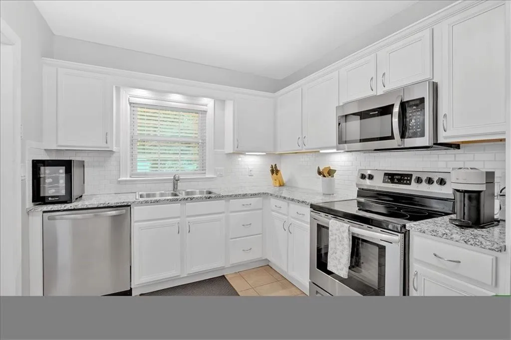Kitchen featuring stainless steel appliances, a sink, white cabinets, decorative backsplash, and light stone countertops