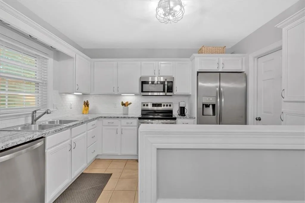 Kitchen with appliances with stainless steel finishes, a sink, white cabinetry, and decorative backsplash