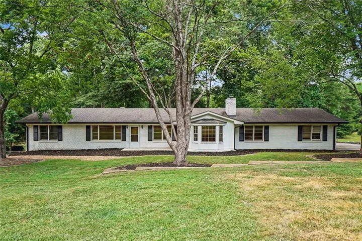 Ranch-style residence featuring a white brick exterior, black window shutters, a prominent bay window, and a central white brick chimney