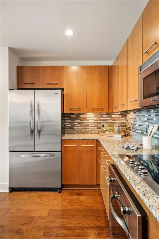 Kitchen with light wood-type flooring, light stone counters, decorative backsplash, and recessed lighting