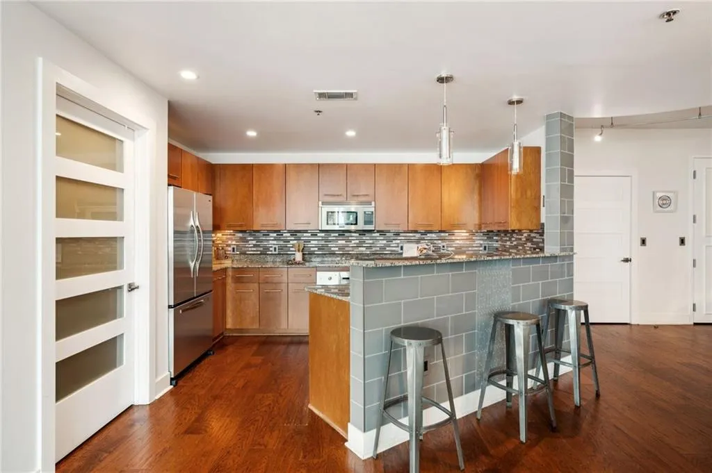 Kitchen featuring stainless steel appliances, dark wood-style flooring, backsplash, a breakfast bar, and brown cabinetry