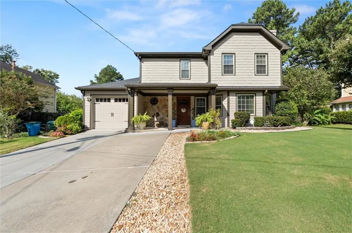 Two-story residence featuring a covered front porch with stone accents, an attached garage, a concrete driveway, and a landscaped front yard