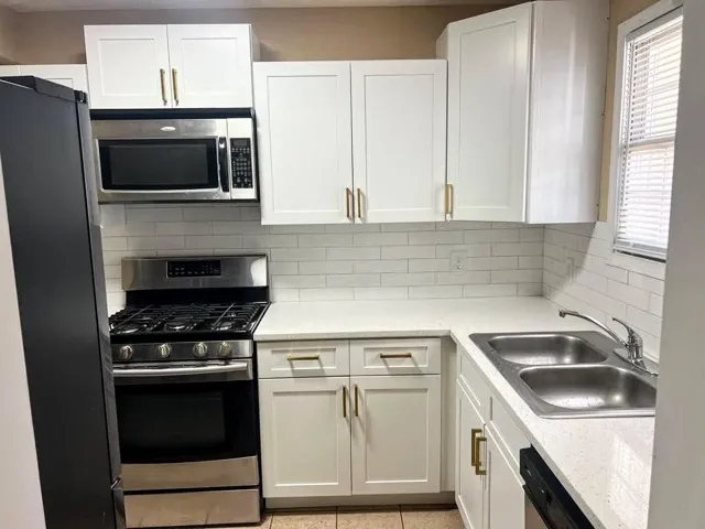White cabinetry with gold-finish hardware, stainless steel appliances, white subway tile backsplash, and light-toned countertops