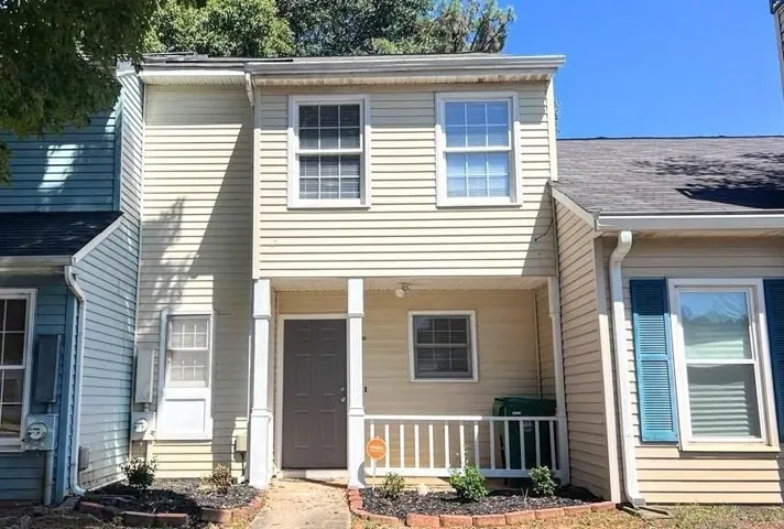 Two-story exterior with light-colored siding, covered front porch, dark-toned entry door, and white window frames