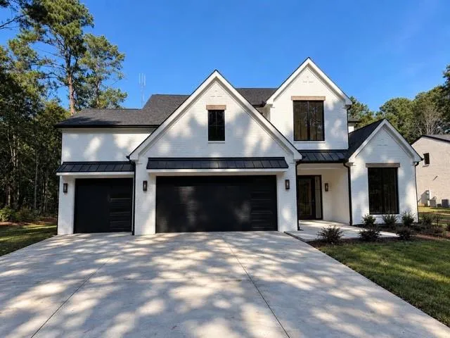 Contemporary exterior with a white brick finish, black framed windows, black garage doors, and a concrete driveway
