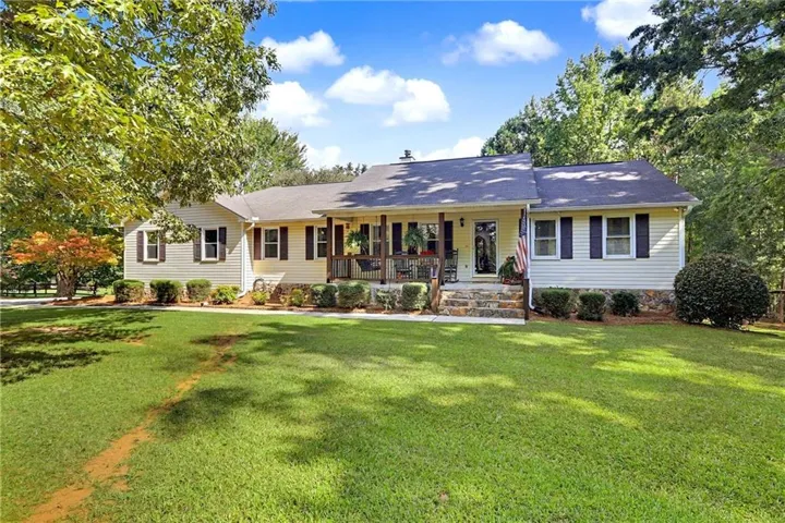 Exterior featuring light-colored siding, dark shutters, and a covered front porch with a wood railing