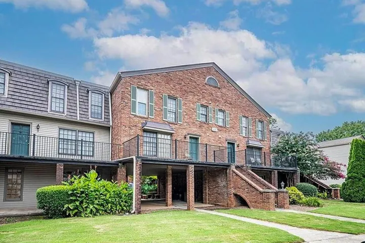 Brick and siding exterior with dormer windows, featuring multiple balconies with metal railings, a brick stairway, and mature landscaping