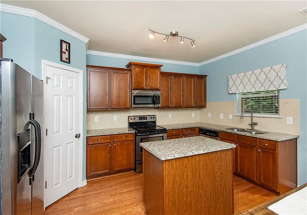 Kitchen with stainless steel appliances, brown cabinets, crown molding, light stone countertops, and light wood-style flooring