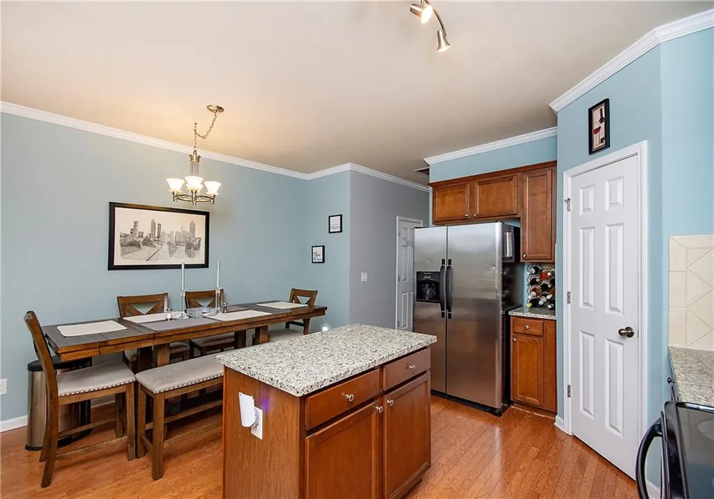 Kitchen featuring crown molding, brown cabinets, light stone countertops, stainless steel refrigerator with ice dispenser, and black stove