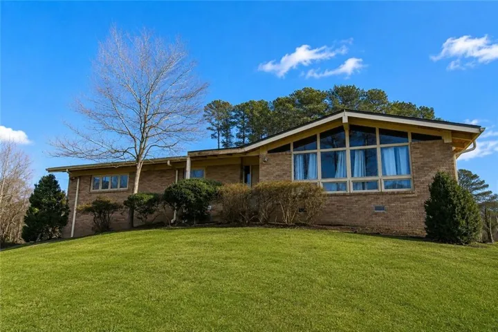 Brick exterior residence situated on a sloped, grassed lot with mature trees