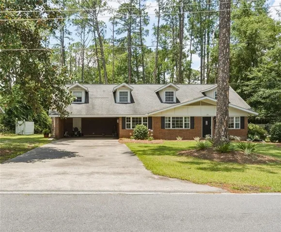 Brick exterior with multiple dormer windows, attached carport, and mature trees