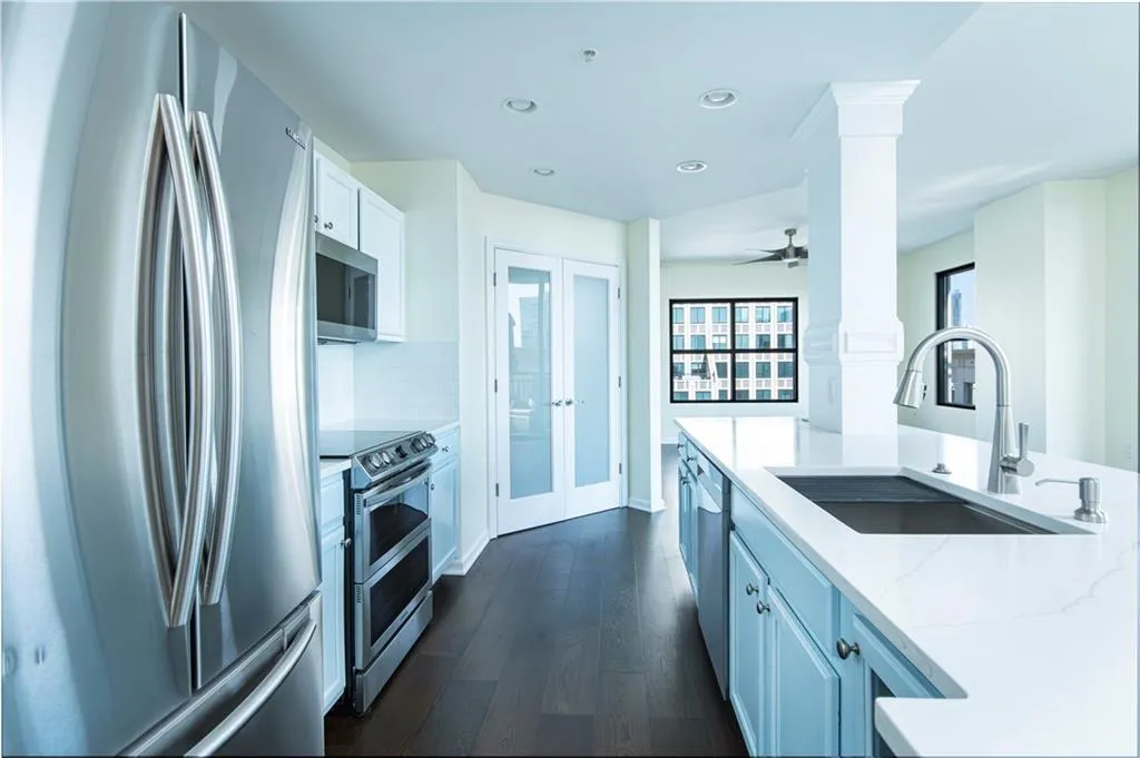 Kitchen featuring stainless steel appliances, ornate columns, white cabinets, dark wood finished floors, and light stone countertops