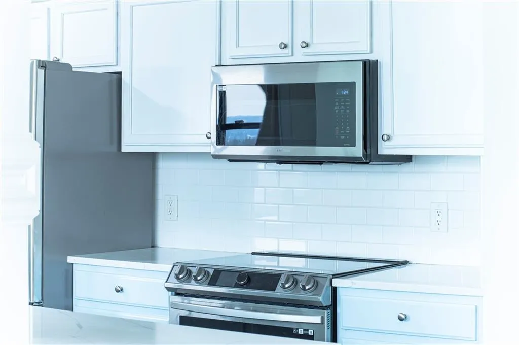 Kitchen featuring stainless steel appliances, white cabinetry, decorative backsplash, and light stone countertops