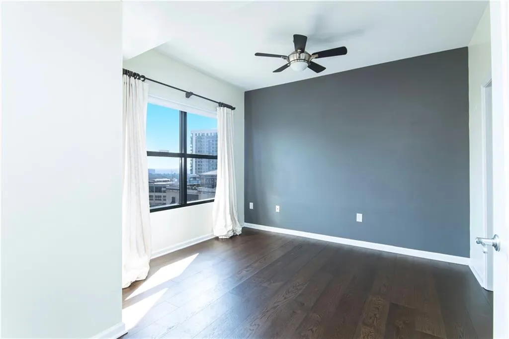 Empty room with a ceiling fan, dark wood-style floors, and a view of city