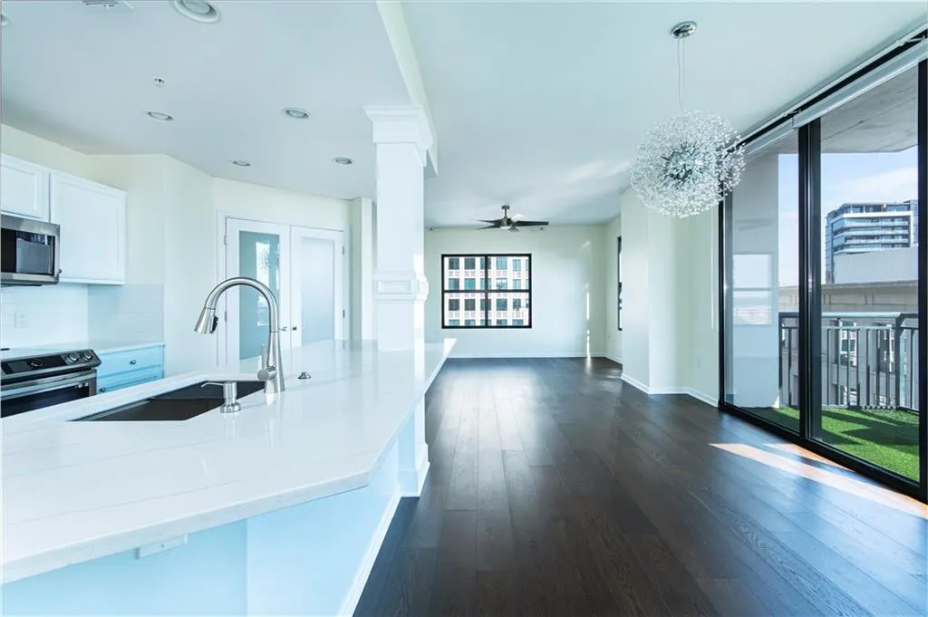 Kitchen featuring stainless steel appliances, open floor plan, white cabinets, decorative columns, and dark wood-style floors